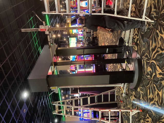 Technician working beside ladders on the frame of a freestanding casino-floor sign.