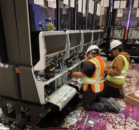 Two technicians servicing open slot machine cabinets during an installation.