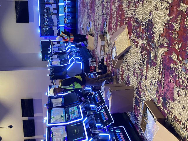 Technicians working along a row of illuminated slot machines during a casino-floor installation.