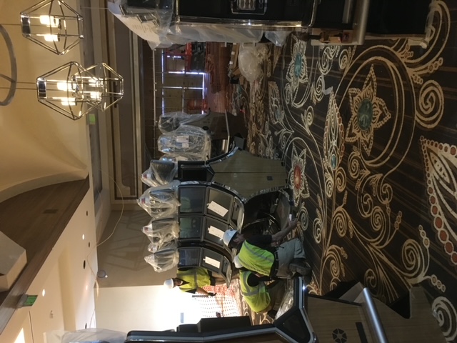 Technicians installing a row of slot machines on a casino floor under construction.